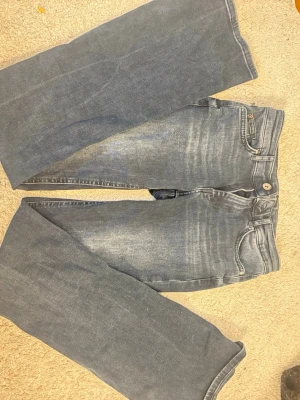 Blå bootcut jeans från ONLY - Säljer ett par blå bootcut jeans från ONLY med klassisk femficksmodell och snygga slitningar framtill. Jeansen har normal midja och dragkedja med knapp. Perfekta för dig som gillar en avslappnad men trendig look.