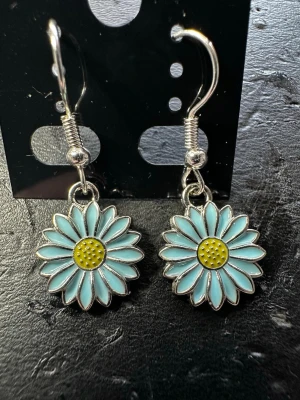 Blå prästkrage örhängen - Snygga örhängen i form av prästkragar med ljusblå kronblad och gul mitt. Hängena är i metall med krokfäste och har en söt, lekfull design som verkligen sticker ut. Perfekta för dig som gillar blommiga accessoarer och vill addera lite färg till din stil.