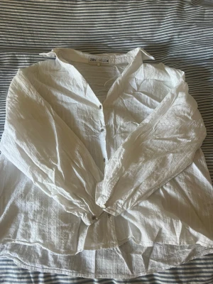 Vit skjorta från Zara med knappar - Luftig vit skjorta från Zara med klassisk krage och knäppning framtill. Skjortan har lång ärm och är tillverkad i ett lätt, strukturerat tyg som ger en avslappnad känsla. Perfekt att styla till jeans eller kjol.