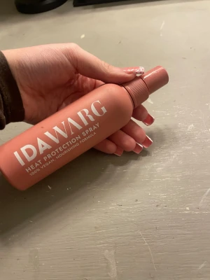 IDAWARG Heat Protection Spray - Värmeskyddsspray från IDAWARG i en matt, rosa plastflaska med vitt tryck. Sprayen är 100% vegansk och har en närande formula som skyddar håret mot värmeverktyg. Praktisk sprayfunktion för enkel applicering.