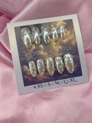 PearlDrip (XS);Medium Almond - Unika handgjorda press-on naglar i pärlemorskimrande vitt med små pärlor som dekoration. Naglarna har en medium längd och almondform och ger en lyxig och trendig look. Perfekta för dig som vill sticka ut med handgjorda detaljer.XS: 14 mm, 11 mm, 11,5 mm, 10 mm, 8 mm 