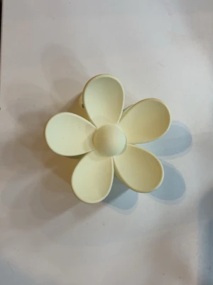 Gul hårklämma i blomform - Söt hårklämma i form av en blomma med fem kronblad i ljusgul plast. Perfekt för att ge en lekfull touch till din frisyr. Klämman är lätt och smidig att använda för att snabbt sätta upp håret.