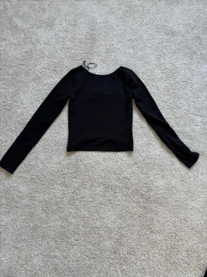 Svart långärmad topp med rund hals - En enkel och stilren svart långärmad topp med rund halsringning. Toppen är croppad och har en slim passform som framhäver siluetten. Perfekt att matcha med jeans eller kjol för en clean look.