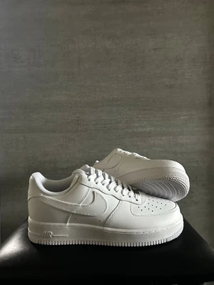 Nike Air Force 1 vita sneakers - Klassiska helvita Nike Air Force 1 sneakers i lågt utförande. Skorna har en stilren design med perforerad tå, kraftig sula och ikoniska Swoosh-loggan på sidan. Tillverkade i läder med textilfoder och snörning framtill. Perfekta för dig som gillar clean och tidlös stil.