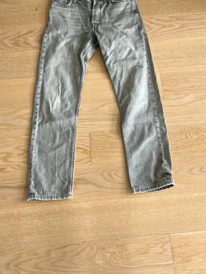 Grå raka jeans från Jack & Jones - Snygga grå jeans från Jack & Jones med rak passform och klassisk femficksdesign. Jeansen har en cool tvättad look och är tillverkade i slitstark denim. Perfekta för dig som gillar en avslappnad men trendig stil.