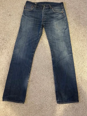 Blå raka jeans från Levi's - Klassiska blå jeans från Levi's med rak passform och fem fickor. Jeansen har en snygg tvättad look och är tillverkade i slitstark denim. Perfekta för en avslappnad stil och passar till det mesta. Levi's-logga på bakfickan. Storlek: W32 L32