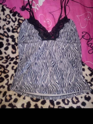 Zebramönstrad spetslinnetopp - Snygg zebramönstrad linnetopp med tunna axelband och svart spetsdetalj vid urringningen. Toppen har en v-ringad form och är perfekt för dig som gillar djurmönster och vill ha något extra till din outfit. Små nopprig. Säljer på vinted också