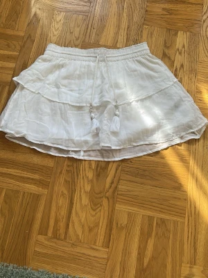 Vit volangkjol med snörning - Säljer en vit  kortkjol med volang och snörning i midjan med tofsar från Gina tricot.💕💕Kjolen har en luftig och lätt känsla💕💕 Resår i midjan för skön passform och dubbla lager tyg för extra volym.💕💕I mycket bra skick💕💕Nypris är ca 250 kr, jag säljer den för 75 kr💕💕Hör av er vid intresse 💕💕