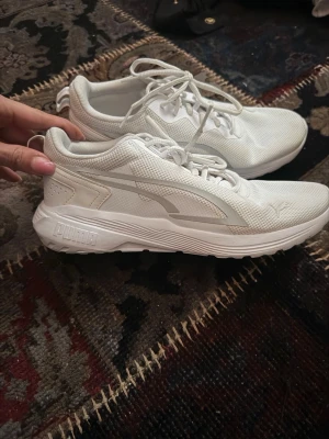 Vita sneakers från Puma - Snygga vita sneakers från Puma med klassisk logga på sidan och tå. Skorna har en låg profil, mesh-överdel för bra andningsförmåga och en rejäl sula för extra komfort. Perfekta för dig som gillar stilrena och sportiga skor.