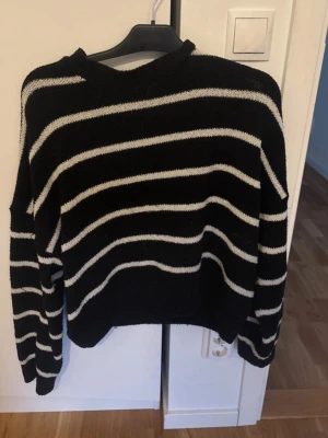 Svart stickad tröja med vita ränder - Säljer en svart stickad tröja med vita horisontella ränder. Tröjan har en avslappnad passform, rund halsringning och långa ärmar. Perfekt för dig som gillar en enkel men snygg stil.