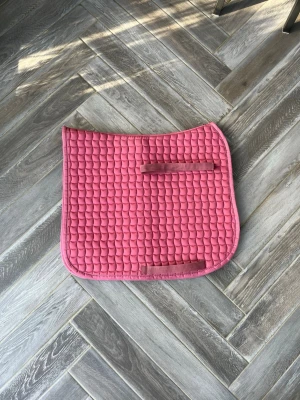Rosa schabrak från Eskadron - Passar en medelstor pony, skriv för mer info om mått! Säljer ett rosa dressyr schabrak från Eskadron med quiltat mönster och två kardborreband för enkel fastsättning. Schabraket har en mjuk och vadderad känsla, perfekt för att ge extra komfort under sadeln. Märket syns tydligt på ena sidan.