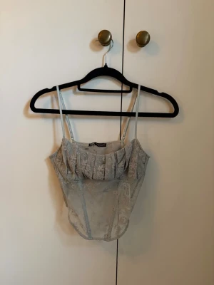 Ljusblå spetskorsett  - Trendig ljusblå korsett från ZARA med tunna axelband och transparent spetsmaterial. Perfekt för att lyfta vilken outfit som helst. Står M men är mer en XS/S