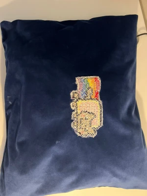 EGENGJORD blå sammetskudde med broderi - Mysig blå kudde i sammetsmaterial med ett broderat motiv av en hand som håller ett regnbågsfärgat objekt på framsidan. Kudden är mjuk och har en unik design som sticker ut i soffan eller på sängen.