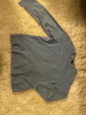 Ljusblå stickad tröja med ribbade muddar - En stilren ljusblå stickad tröja med breda ribbade muddar vid ärmslut och nederkant. Tröjan har rund halsringning och är tillverkad i ett mjukt, tunt material som känns skönt mot huden. Perfekt för lager på lager och enkel att matcha.