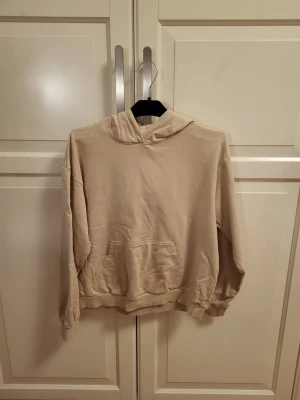 Beige oversized hoodie med ficka - En beige oversized hoodie med stor känguruficka framtill och huva. Hoodien har ribbade muddar vid ärmslut och nederkant. Perfekt för en avslappnad och chill stil.