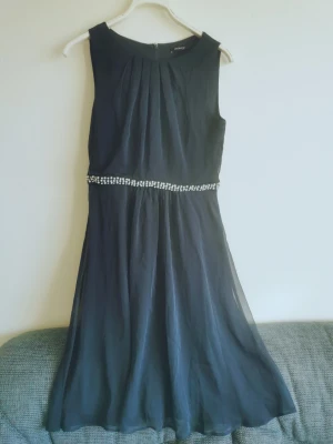 Orsay klänning med pärldetalj - Orsay knälång fodrad ärmlös klänning med pärldetalj i midjan. Polyester. Står som storlek 38 men känns som 34 eller 36. Gott skick, inga skador eller fläckar. 