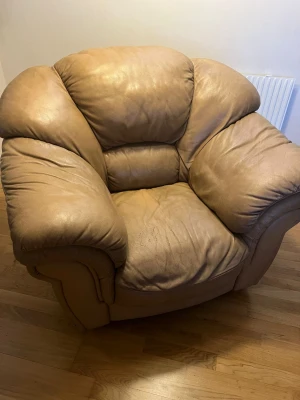 Stor mörkbeige skinnfåtölj (kontakta för upphämtning) - Säljer en rejäl och mjuk fåtölj i mörkbeige skinn med breda armstöd och djup sits. Perfekt för dig som vill ha en riktigt bekväm plats att slappa på. Fåtöljen har en rundad form och är stoppad för extra komfort.