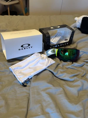 Oakley gröna spegelglas goggles - Säljer ett par Oakley goggles med gröna spegelglas och bred svart/vit rem. Snygg och futuristisk design som ger grym stil i backen. Kommer med originalförpackning och vit förvaringspåse. Perfekta för soliga dagar på fjället. Special linser (PRIZM) linser, ingen repa eller liknande
