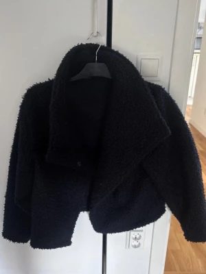 Marinblå teddyjacka med stor krage - Mysig marinblå teddyjacka med oversized krage och tryckknappsstängning. Jackan har en boxig, lite croppad passform och är gjord i fluffigt teddy-material som håller dig varm. Perfekt för dig som gillar en trendig och avslappnad stil. Den översta knappen är av som syns på andra bilden men bortsett från det är den i bra skick och går fortfarande att stänga med dom andra knapparna 