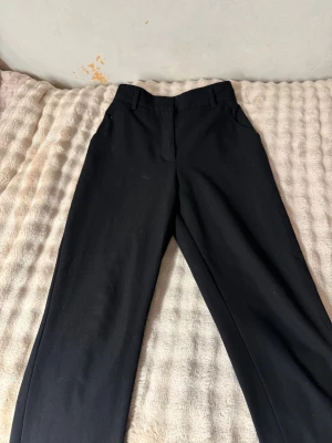 Svarta kostymbyxor med raka ben - Snygga svarta kostymbyxor med raka ben och hög midja. Byxorna har bälteshällor, sidofickor fram och två passpoalfickor bak. Klassisk och stilren design som passar till många olika looks.