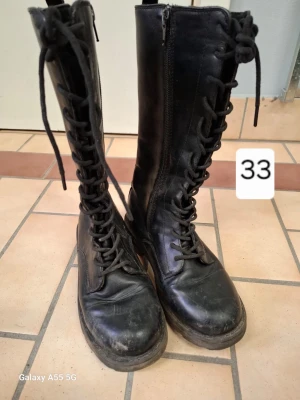 Svarta höga kängor med snörning - Säljer ett par svarta höga kängor med snörning och dragkedja på sidan. Klassisk militärinspirerad look med robust sula och rundad tå. Tillverkade i läder eller konstläder, perfekta för en edgy stil. Passar dig som gillar boots med attityd.