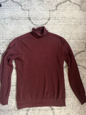 Vinröd polotröja från John Henric - Säljer en vinröd ribbstickad polotröja från John Henric. Tröjan har lång ärm, hög polokrage och är tillverkad i ett mjukt, stretchigt material. Perfekt för lager på lager och en clean look.