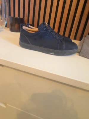 Mörkblå sneakers med röd sula - Snygga mörkblå sneakers med lågt skaft och kontrasterande röd sula. Skorna har klassisk snörning och en stilren design som passar till det mesta. Insidan är ljusbeige och ovandelen verkar vara i mocka eller nubuck. Perfekta för dig som gillar en clean look. Tvättar innan jag skickar