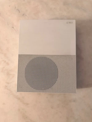 Xbox One S vit spelkonsol - Säljer en Xbox One S spelkonsol i vit färg med stilren, rektangulär design och ventilerad front. Konsolen har HDMI-utgång och nätverksport på baksidan. Perfekt för gaming och streaming, snygg att ha framme i vardagsrummet.