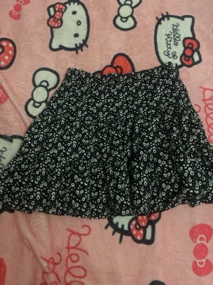 Svart blommig kortkjol från 157 New - Supersöt svart kortkjol från 157 New med vitt blommönster. Kjolen har en lätt utställd form och elastisk midja för skön passform. Perfekt att matcha med en enkel topp eller hoodie för en chill look.