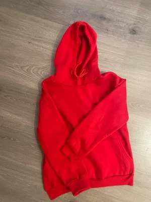 Röd hoodie med huva och ficka - Säljer en klassisk röd hoodie med huva. Hoodien har en stor magficka och ribbade muddar vid ärmslut och nederkant. Perfekt för en avslappnad och stilren look. Materialet känns mjukt och bekvämt. Lappen saknas tyvärr så vet inte var den är köpt. Säljer då den e för liten.