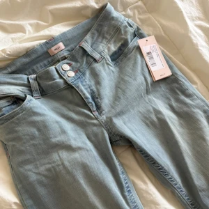 Ljusblå jeans  - Säljer ett par helt nya jeans från Nelly.  Jeansen har coola bakfickor med rosa broderade detaljer i zigzag-mönster.  Storlek 40/Short. Nypris är 699kr