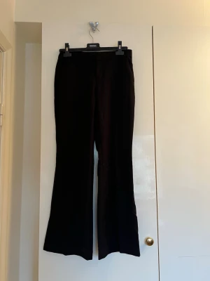 Svarta kostymbyxor från GinaTricot - Snygga svarta kostymbyxor från GinaTricot med låg midja och lätt utsvängda ben. Byxorna har bälteshällor och en diskret bakficka. Perfekta för en stilren och modern look. Materialet känns mjukt och har en elegant finish.