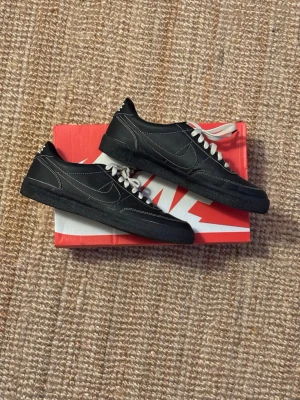 Nike killshot 2 Leather - Säljer ett par svarta Nike sneakers med vita kontrastsömmar och vita skosnören. Skorna har en låg profil och klassisk design med NIKE-logga på hälen. Materialet är en mix av läder och syntet, perfekt för dig som gillar stilrena och tidlösa sneakers.