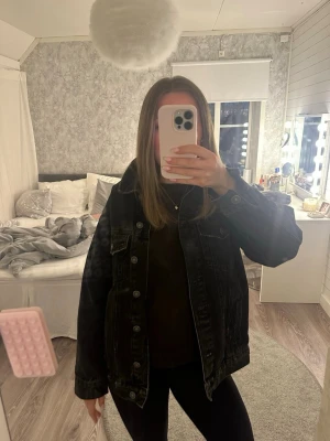 Svart oversized jeansjacka från Bershka - Säljer en svart oversized jeansjacka från bershka med klassisk krage, knappstängning framtill och två bröstfickor med lock. Jackan har en avslappnad passform och slitna detaljer för en cool look. Perfekt att slänga över en hoodie eller t-shirt.