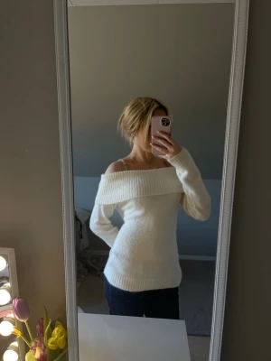 Vit off shoulder stickad tröja - Säljer en vit stickad tröja med bred off shoulder-krage. Tröjan har lång ärm och ribbstickade muddar vid ärmslut och nederkant. Perfekt för dig som gillar en avslappnad men trendig stil.