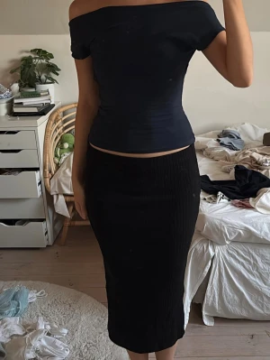 Svart långkjol i ribbad bomull - Säljer en svart långkjol med ribbad struktur. Kjolen har en tight passform och är gjord i mjuk bomull som sitter skönt mot kroppen. Perfekt att styla med en crop top eller en oversized tröja. 