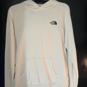 Vit hoodie från The North Face - Vit hoodie från The North Face med svart logga på bröstet och stort tryck på ryggen med texten 'Never Stop Exploring'