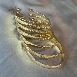 Guldiga armband med mönster - Säljer flera guldiga armband i olika modeller med snygga ingraverade mönster och detaljer. Några har tvinnad design och små kulor i ändarna. Perfekta att mixa och matcha för en trendig look.