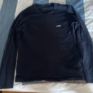 långärmad tröja BOSS - Svart långärmad tröja från BOSS med vit broderad logga på bröstet. Klassisk rund halsringning och stilren design, perfekt för en clean och enkel look. Tillverkad i mjuk bomull som känns skön mot huden.