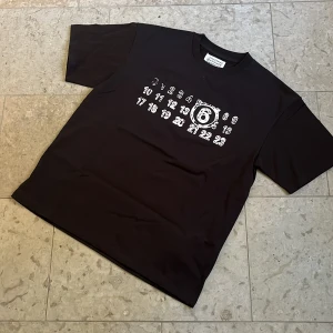 Maison Margiela T-shirt med tryck - Svart t-shirt från Maison Margiela med vit logotyptryck på bröstet i storlek S, T-shirten är i toppskick och fraktas inom 24h✅