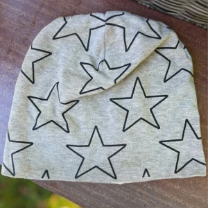Grå mössa med svarta stjärnor H&M - Grå mössa från H&M i storlek 110/128, dekorerad med stora svarta stjärnor över hela ytan. Tillverkad i mjuk bomull, perfekt för att hålla värmen under kyliga dagar. Snygg och enkel design som passar till det mesta.