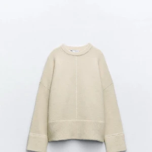 Beige stickad tröja från Zara - Mysig beige stickad tröja från Zara med rund halsringning och breda muddar vid ärmslut och nederkant. Tröjan har en relaxed fit och en diskret söm mitt fram som ger en stilren look. Perfekt för lager-på-lager under kyliga dagar.