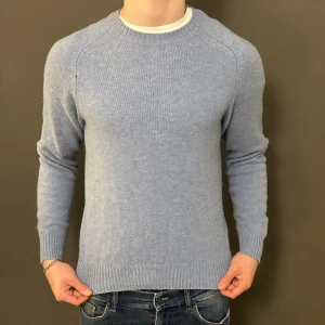 Ljusblå stickad tröja med rund hals - Snygg ljusblå stickad tröja med rund hals och ribbade muddar vid ärmslut och nederkant. Modellen är klassisk och passar perfekt till jeans. Tröjan har lång ärm och är mjuk i materialet, vilket gör den skön att bära under kyliga dagar.
