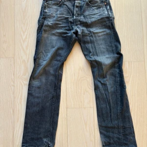 Levi's 501 svarta jeans straight fit - Klassiska Levi's 501 jeans i svart med slitningar och hål vid benslutet och skrevet. Rak passform och normal midja.