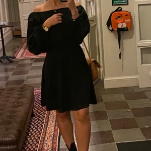 Svart offshoulder klänning - Supersnygg svart kortklänning med offshoulder-modell och långa puffärmar. Klänningen har resår i midjan och knäppning vid ärmsluten. 