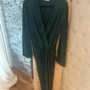Mörkgrön långklänning med v-ringning - Supersnygg mörkgrön långklänning från NA-KD med plisserat tyg, djup v-ringning och vida långa ärmar. Klänningen har omlottkänsla upptill och markerad midja. Perfekt för dig som vill sticka ut med en elegant och trendig look.