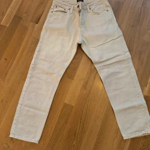 Beige jeans från Jack & Jones, relaxed fit - Beiga jeans från Jack & Jones i modellen Relaxed-Chris. De har en avslappnad passform, raka ben och klassiska fem fickor. Tillverkade i bomull med snygga metallnitar och knappgylf. Perfekta för en chill och stilren look.