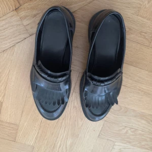 Svarta loafers med fransdetalj - Stilrena svarta loafers i blankt skinn med klassisk fransdetalj framtill. 