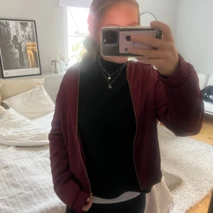 Vinröd bomberjacka - Säljer en snygg vinröd bomberjacka med dragkedja. Jackan har långa ärmar och en stilrent design som passar perfekt för höst, vår och även lite kallare sommarkvällar. Köpte på sellpy ”nytt skick” och har inte använt sedan dess. Hör av er vid mer frågor.