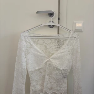 Vit spetsblus med v-ringning - Säljer en vit långärmad blus i spets med v-ringning och fina spetsdetaljer.  Oanvänd men ingen prislapp kvar